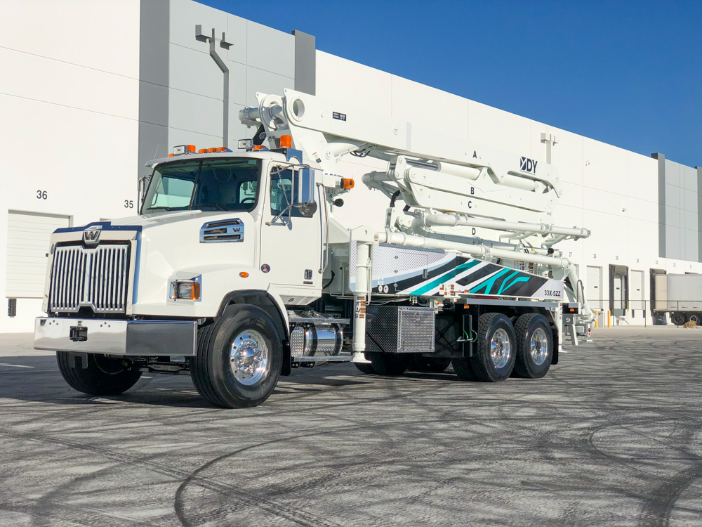 DY Concrete Pumps boom pump with teal, white, and black design outside of the WOC event